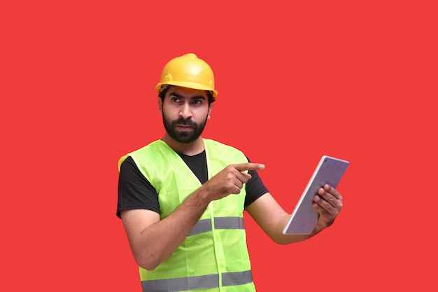 Young construction worker holding tab and pointing it indian\
pakistani model