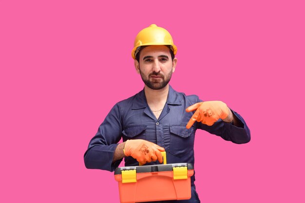 young construction worker holding tool box and pointing it indian pakistani model