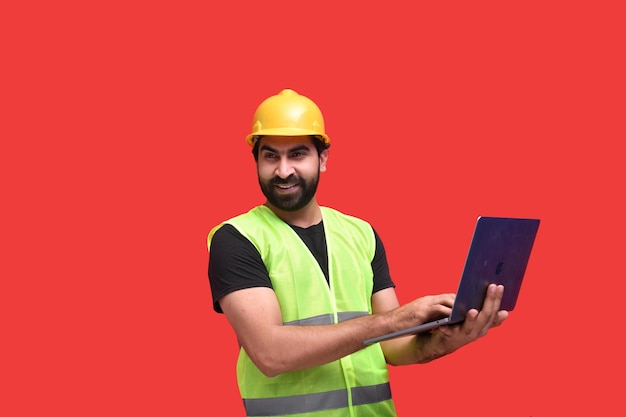 Молодой строитель улыбается, держа ноутбук индийская пакистанская модель