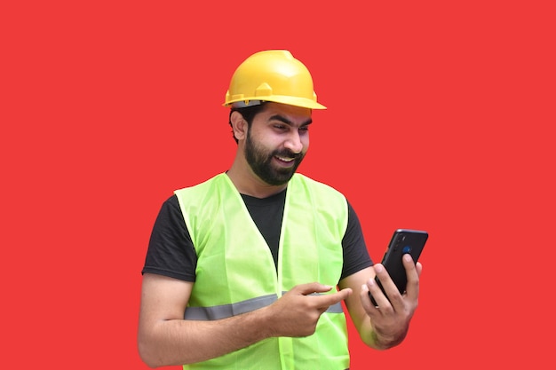 Young construction worker smiling holding phone and pointing it\
indian pakistani model