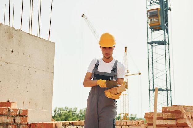 Young construction worker in uniform is busy at the unfinished building