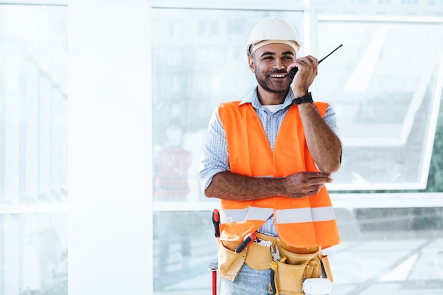 Giovane operaio edile in uniforme che utilizza un walkie-talkie sul posto