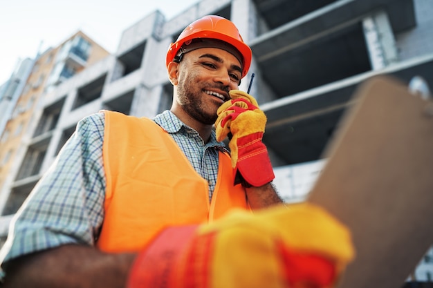 Young construction worker in uniform using walkie talkie on site