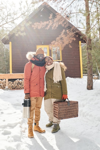 Young contemporary couple with luggage standing against their country house