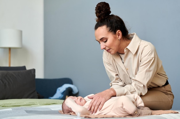 Young contemporary female in smart casualwear bending over her baby son