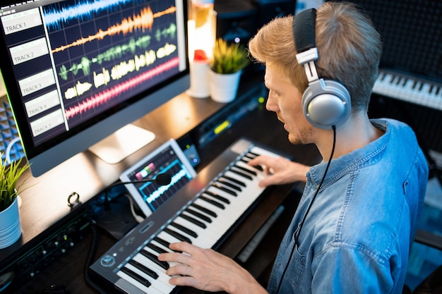 Photo young contemporary musician in headphones recording new music and songs while playing on piano keyboard in studio