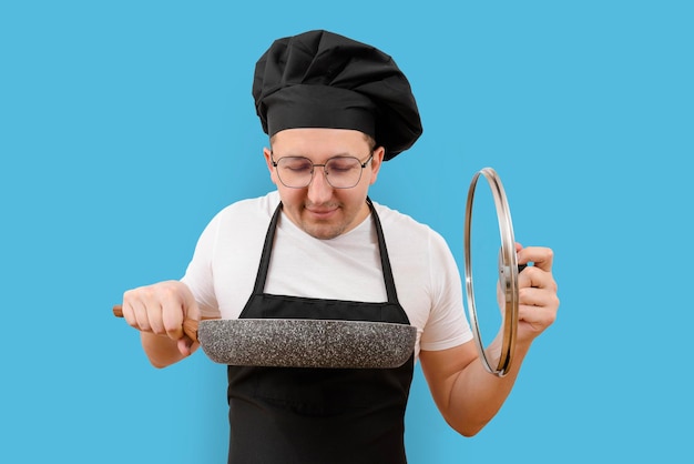 Молодой повар со сковородой в руке на синем фоне Концепция приготовления пищи