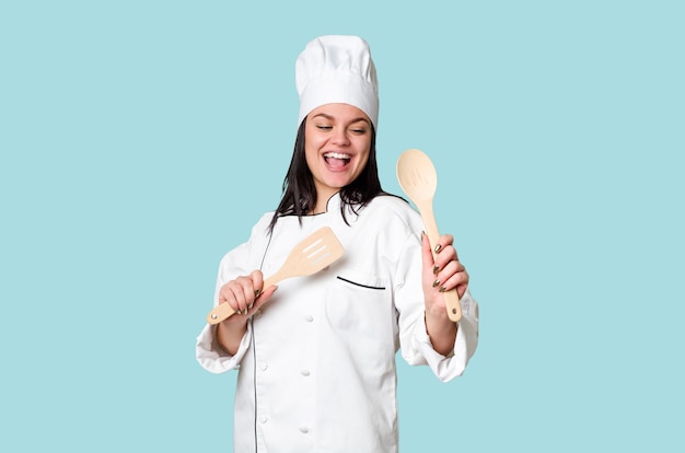 Young cook woman holding wooden spoon and fork isolated