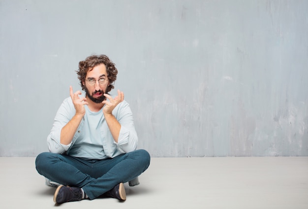 Young cool bearded man sitting on the floor. grunge wall background