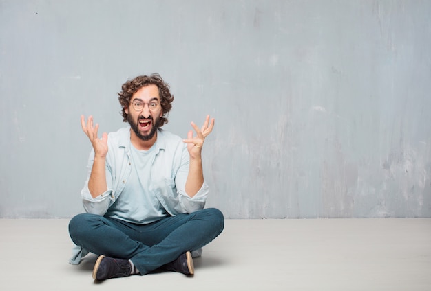 Young cool bearded man sitting on the floor. grunge wall background