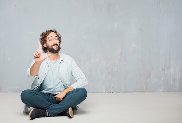 Young cool bearded man sitting on the floor. grunge wall background