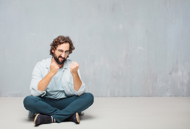 Young cool bearded man sitting on the floor. grunge wall background