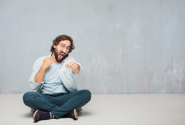 Young cool bearded man sitting on the floor. grunge wall background