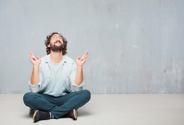 Young cool bearded man sitting on the floor. grunge wall background