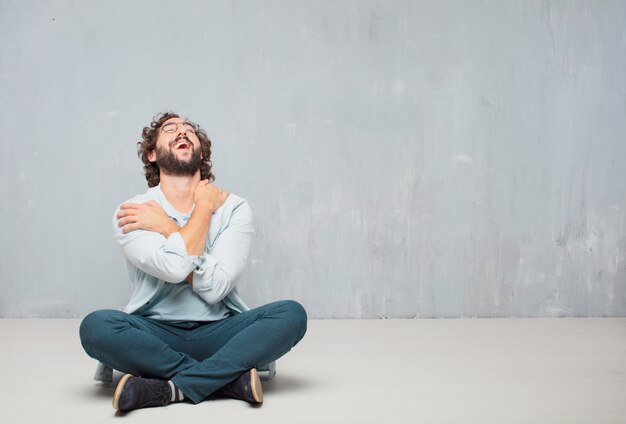 Young cool bearded man sitting on the floor. grunge wall background