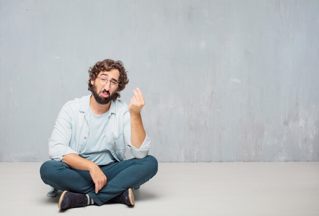 Young cool bearded man sitting on the floor. grunge wall background