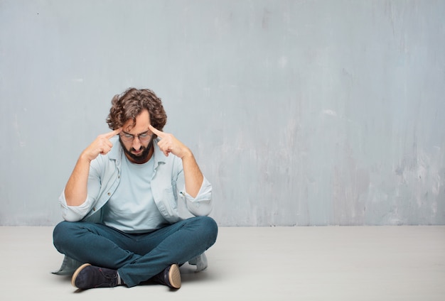 Young cool bearded man sitting on the floor. grunge wall background