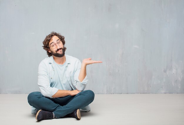 Young cool bearded man sitting on the floor. grunge wall background