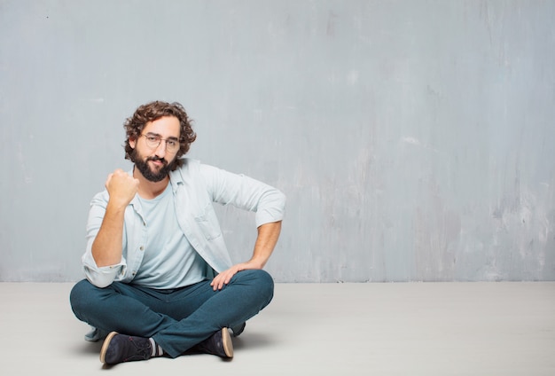 Young cool bearded man sitting on the floor. grunge wall background