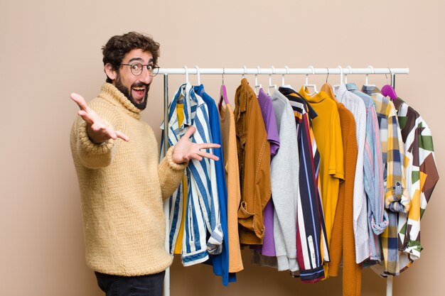 Young cool berded man with clothes against flat wall