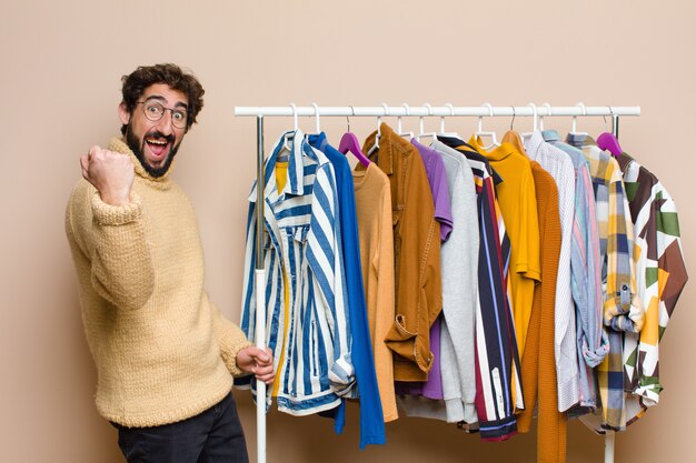 Young cool berded man with clothes against flat wall