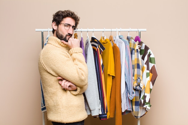 Young cool berded man with clothes against flat wall