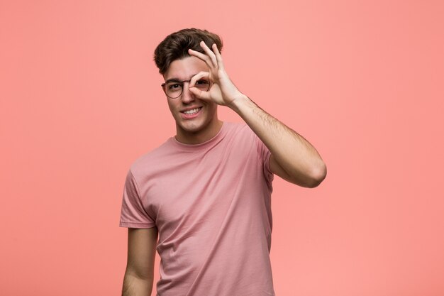 Young cool caucasian man excited keeping ok gesture on eye.