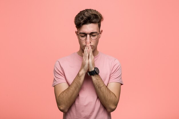 Young cool caucasian man holding hands in pray near mouth, feels confident.
