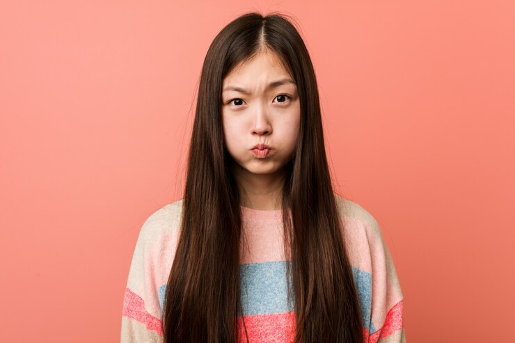 Photo 若いクールな中国人女性は頬を吹く、疲れた表情をしています。顔の表情のコンセプト。