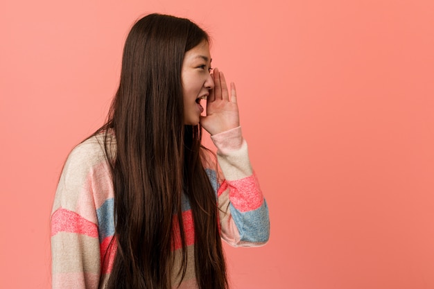 Young cool chinese woman shouting and holding palm near opened mouth.