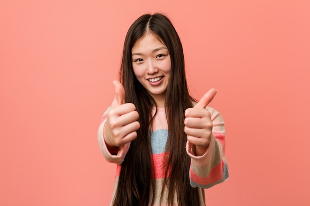 Young cool chinese woman with thumbs ups, cheers about something, support and respect concept.