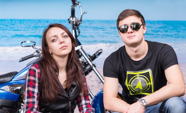 Young Cool Couple Looking Tough Crouching in front of Motorcycle on Beach