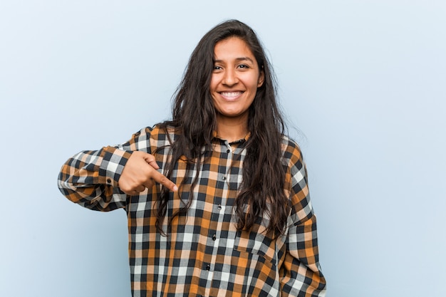 Young cool indian woman person pointing by hand to a shirt copy space, proud and confident