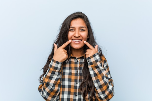 Young cool indian woman smiles, pointing fingers at mouth.