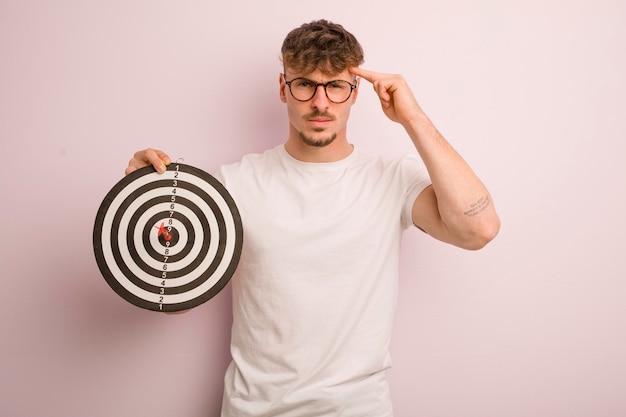 Young cool man feeling confused and puzzled showing you are insane dart target concept