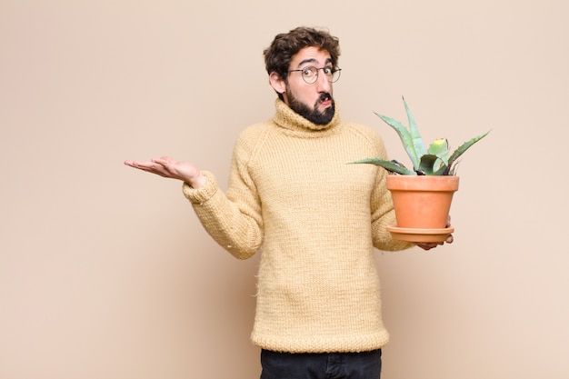 Young cool man holding a cactus plant against flat wall