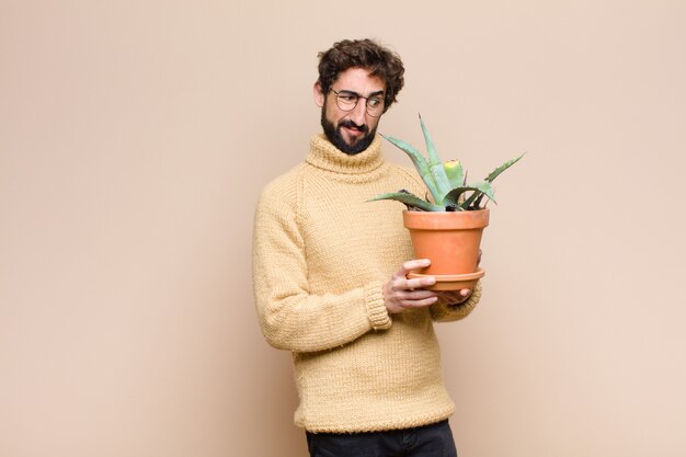 Giovane uomo freddo che tiene una pianta di cactus sopra la parete