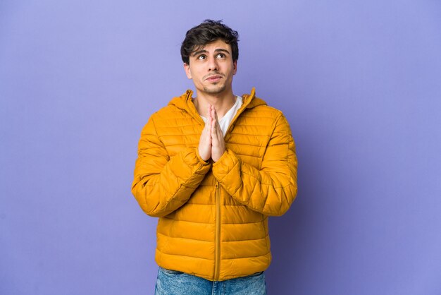 Young cool man holding hands in pray near mouth, feels confident