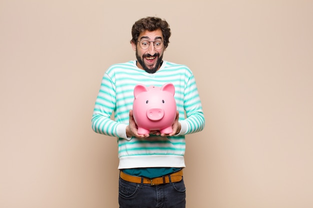 Young cool man holding a piggy bank against clean wall