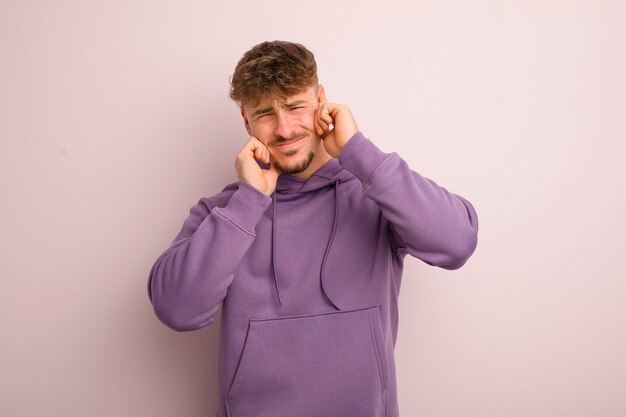 Young cool man looking angry stressed and annoyed covering both ears to a deafening noise sound or loud music