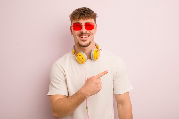 Young cool man looking excited and surprised pointing to the side sunglasses and headphones