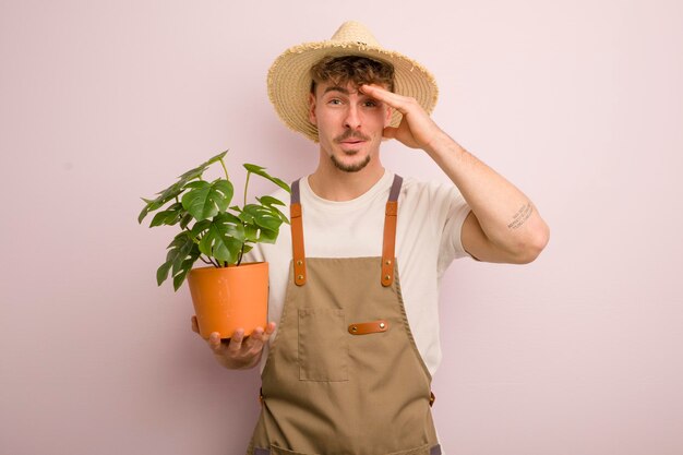 Young cool man looking happy astonished and surprised gardener and plant