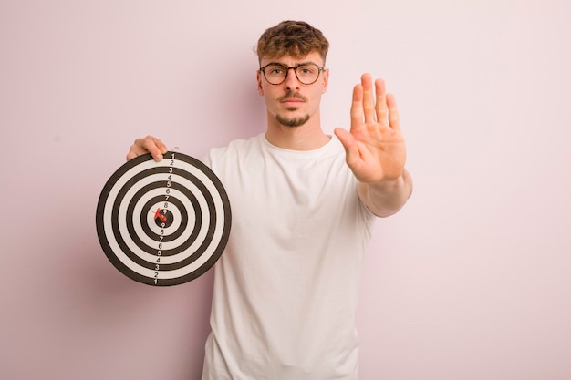 Young cool man looking serious showing open palm making stop gesture dart target concept