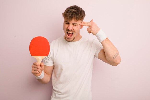 Young cool man looking unhappy and stressed suicide gesture making gun sign pingpong concept