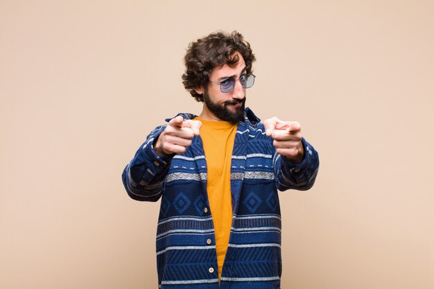 Young cool man pointing forward at camera with both fingers and angry expression, telling you to do your duty against wall