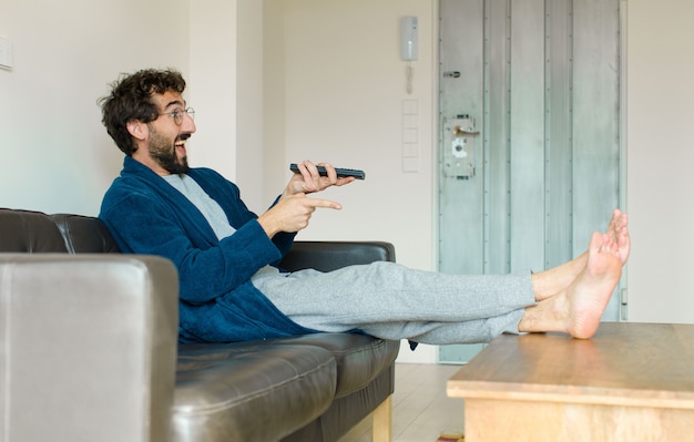 Young cool man sitting on a sofa at living room watching tv