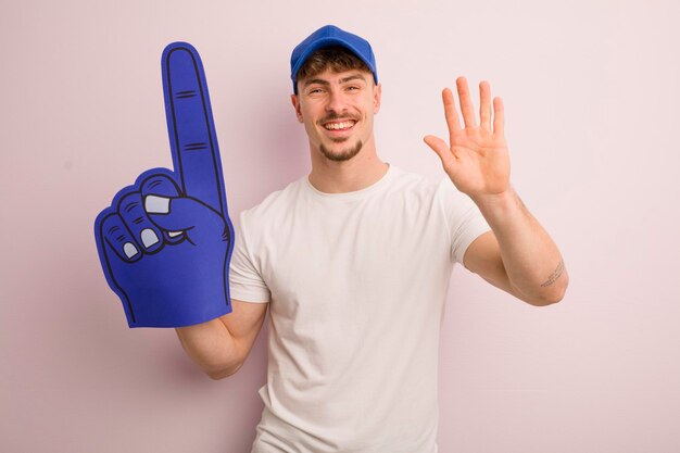 Young cool man smiling happily waving hand welcoming and greeting you number one fan concept