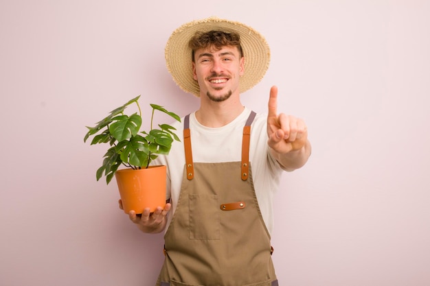 誇らしげにそして自信を持って笑顔の若いクールな男は、ナンバーワンの庭師と植物を作ります