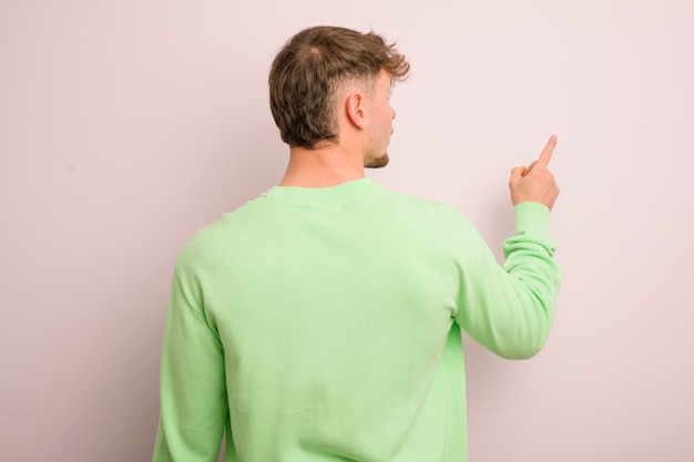 Young cool man standing and pointing to object on copy space rear view