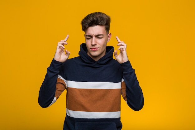 Young cool man wearing a hoodie crossing fingers for having luck